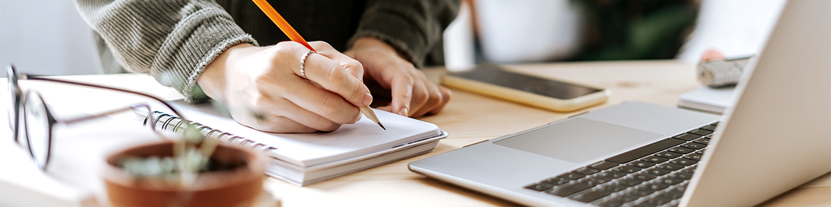 woman writing on notepad next to laptop in spring