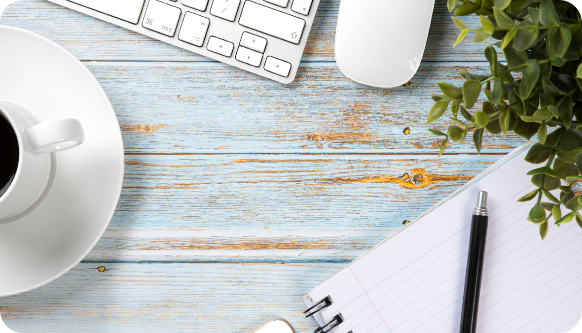 overhead view of a coffee cup, keyboard, notepad on a wooden table top